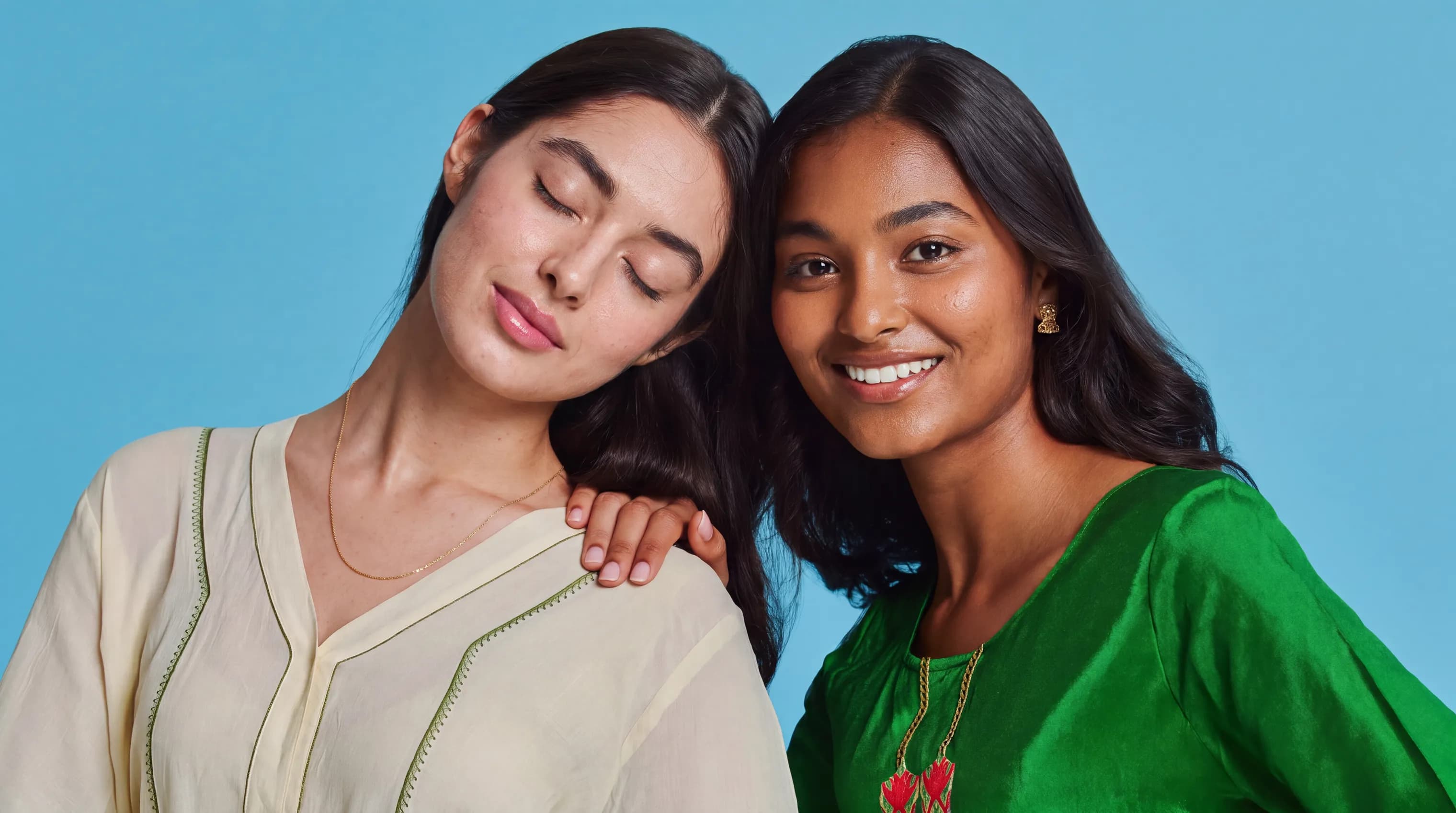 Two smiling friends with freckles, bright makeup, light blue background